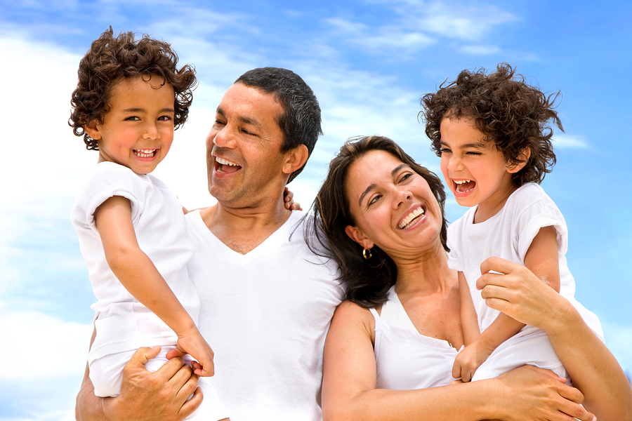 A happy family of four laughing together under a bright blue sky